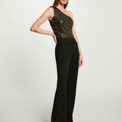 Mulher vestindo top dourado brilhante de um ombro e calças pretas de corte reto