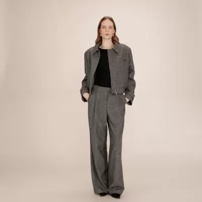 Mulher vestindo casaco e calças cinzentas largas com t-shirt preta em fundo neutro