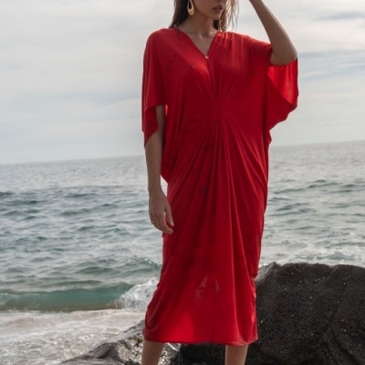 Mulher com vestido vermelho comprido com decote em V em cima de rochas junto ao mar