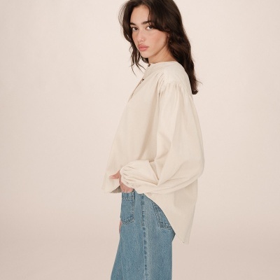 Blusa creme de mangas compridas com calças de ganga azuis em fundo branco.