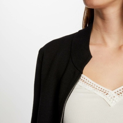 Mulher com casaco preto e camisola branca com detalhes em renda no decote