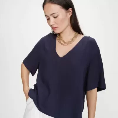 Mulher com t-shirt azul marinho de manga curta e decote em V, calças brancas e colar dourado