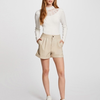 Mulher vestindo blusa branca rendada e calções bege com sapatilhas brancas