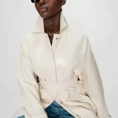 Casaco creme brilhante com cinto e botões grandes usado com jeans e óculos de sol pretos