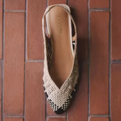 Sandália feminina entrelaçada de couro bege com detalhes pretos sobre piso de ladrilhos vermelhos