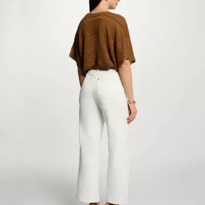 Mulher de costas com top castanho, calças brancas largas e sandálias de salto alto castanhas