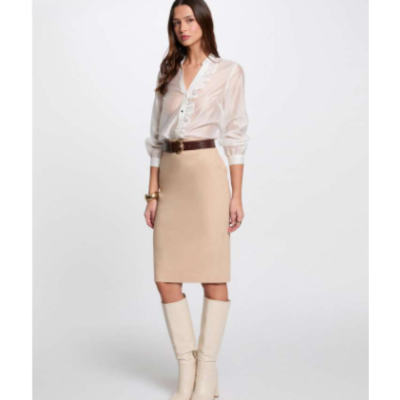 Mulher com camisa branca semi-transparente, saia lápis bege, cinto castanho e botas bege.