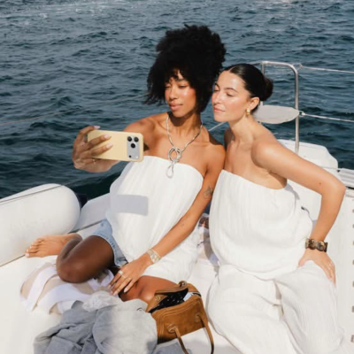 Duas mulheres em roupas brancas em barco com mar ao fundo.
