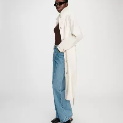 Mulher com casaco creme, calças de ganga azuis e óculos escuros