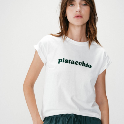 Mulher com t-shirt branca com texto verde e calças verde escuras.