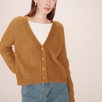 Mulher com cardigan castanho e jeans azuis em fundo creme