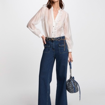 Mulher com camisa branca semitransparente, calças de ganga azul, botas pretas e mala mochila azul