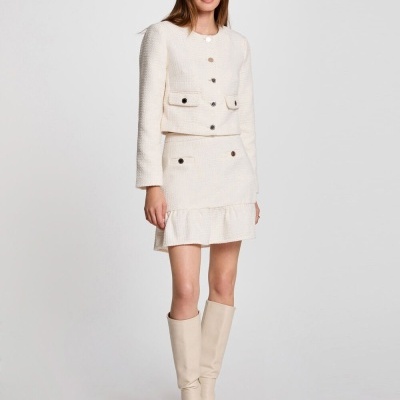 Mulher vestindo conjunto creme de casaco e saia com botões dourados e botas altas creme