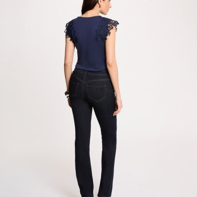 Mulher vista de costas com top azul de renda, jeans escuros e sandálias castanhas em fundo branco