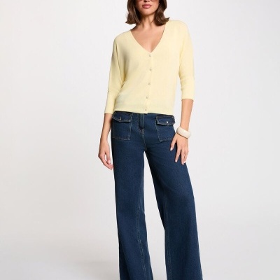 Mulher com cardigan amarelo claro e calças de ganga azul escuro, óculos de sol e botas pretas