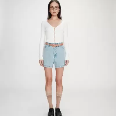 Modelo a usar suéter branco, calções de ganga, meias transparentes e sapatos pretos em fundo branco