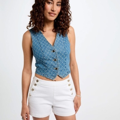 Mulher com colete azul de ganga e calções brancos, em fundo branco.