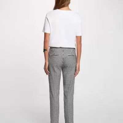 Mulher vista de costas a usar calças xadrez pretas e brancas, t-shirt branca de manga curta e sapatos pretos de salto médio com tiras.