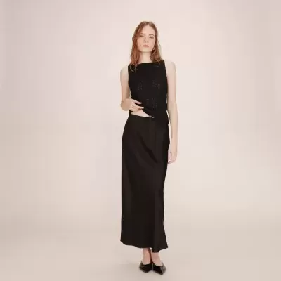 mulher com top preto e saia preta longa em fundo bege