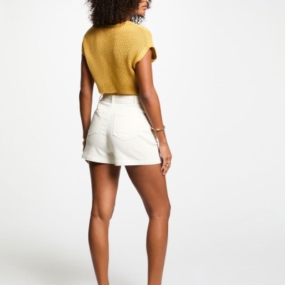 Mulher de costas com t-shirt mostarda, calções brancos e sandálias brancas