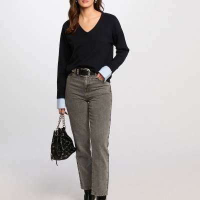 Mulher com camisola preta e golas azuis, jeans cinza, botas pretas e mala preta de correntes