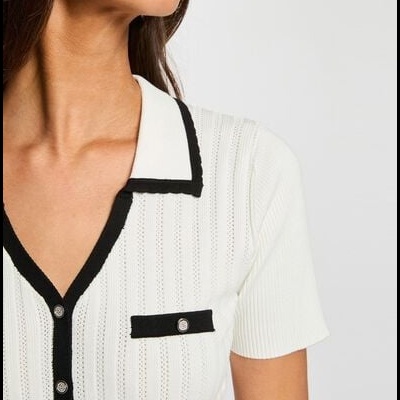 Camisola branca de malha com gola branca e bordas pretas, botões e bolso decorativo.