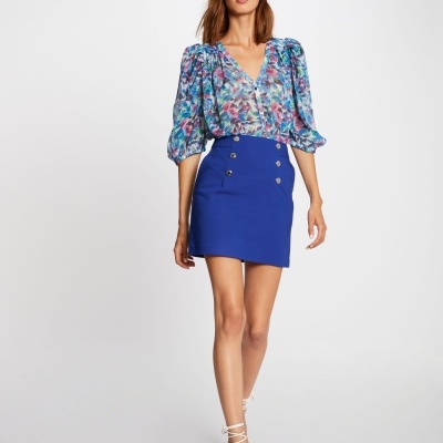 Mulher de blusa floral e saia azul posando em fundo branco