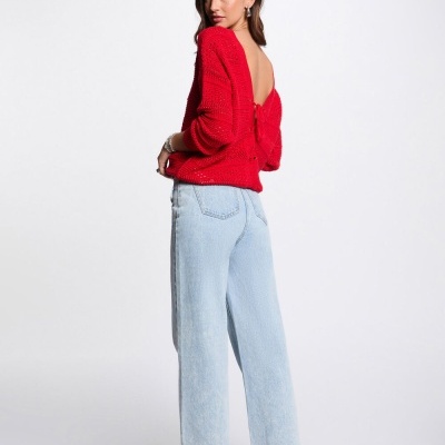 Mulher vestindo camisola vermelha de malha com costas abertas e calças de ganga claras