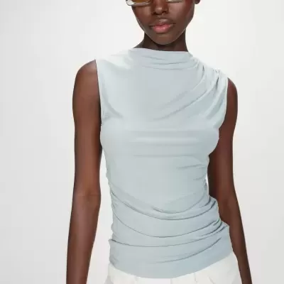 Top azul claro sem mangas com franzidos e óculos de sol amarelos em fundo branco.