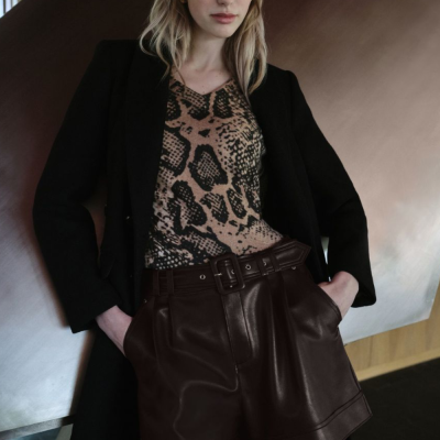 Mulher com casaco preto, camisa animal print e calções de couro castanho escuro