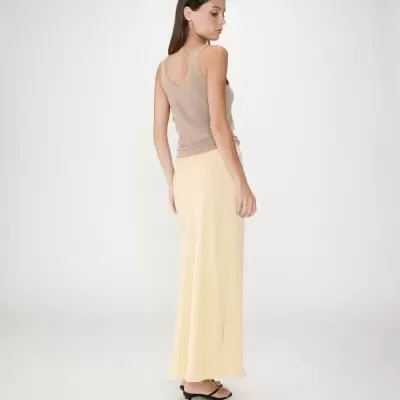 Mulher com camisola bege brilhante, saia amarela comprida e sandálias pretas de salto baixo