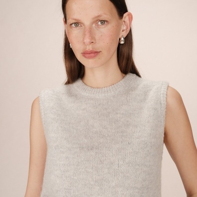 Mulher de cabelo castanho liso com blusa cinza clara sem mangas e gola redonda