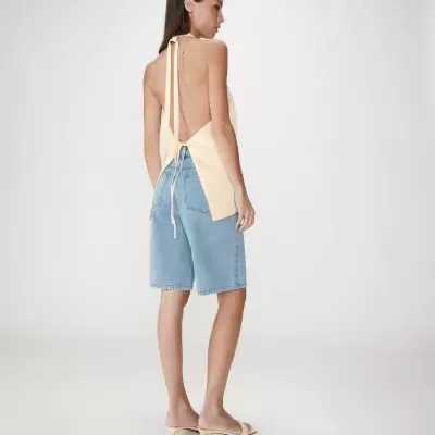 Mulher a usar top amarelo claro sem costas, calções de ganga azul clara e sandálias amarelas.