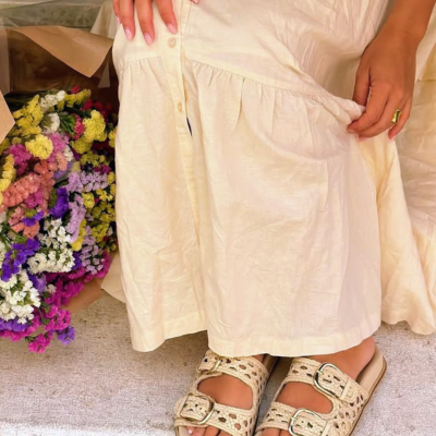 Sandálias bege trançadas com fivelas e vestido creme junto a flores coloridas