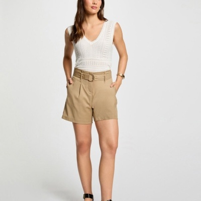 Mulher com top branco rendado e shorts bege com cinto, usando sandálias pretas em fundo branco.