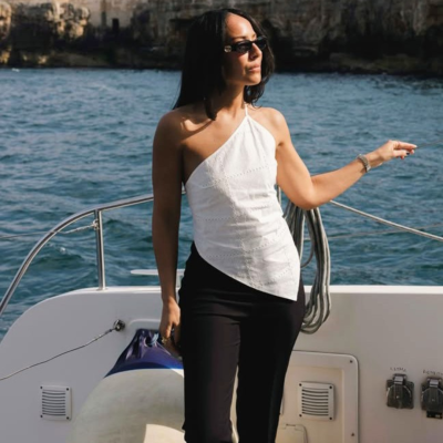 Mulher com top branco assimétrico e calças pretas em barco no mar