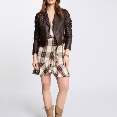 Mulher com vestido xadrez, jaqueta de couro castanha e botas bege num fundo branco.