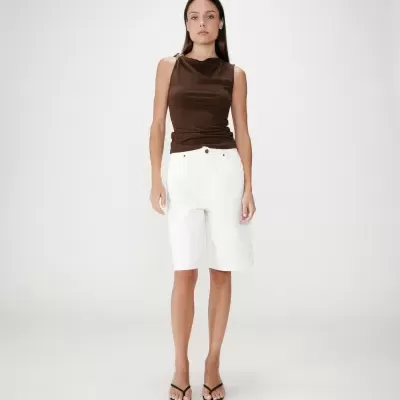 Mulher com top castanho, calções brancos e sandálias pretas em fundo branco