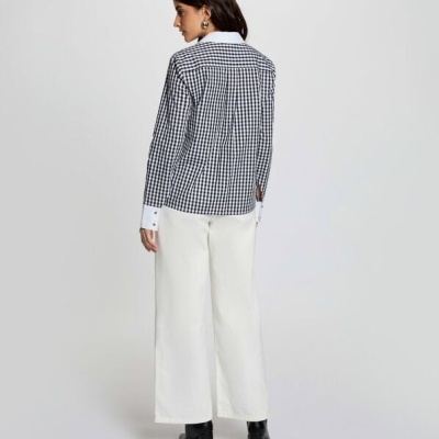 Mulher de costas com camisa xadrez preta e branca e calças brancas largas
