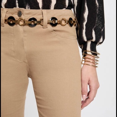 Calças beje com cinto de elos dourados e pretos, blusa padrão ziguezague preto e branco e braceletes dourados