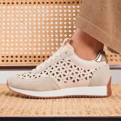 Ténis bege com recortes triangulares e detalhes dourados junto a calças castanhas