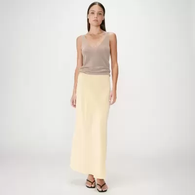 Mulher com top castanho claro de alças finas e saia amarela clara comprida