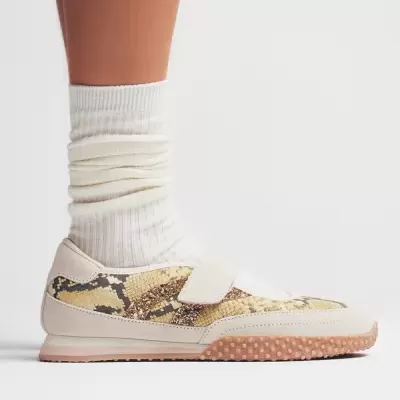 Sapato desportivo bege com padrão de pele de cobra e sola castanha texturada.