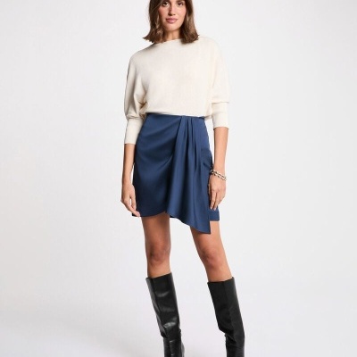 Mulher com camisola branca, saia azul e botas pretas em fundo branco