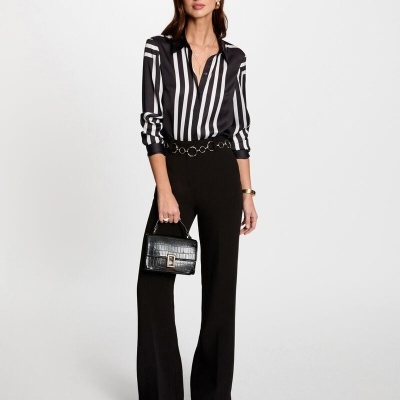 Mulher vestindo camisa riscada preta e branca, calças pretas, sapatos bordeaux e bolsa preta com textura croco