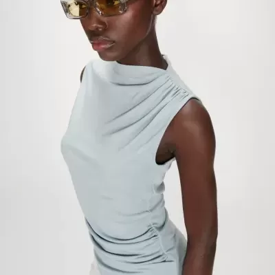 Mulher a usar top azul claro sem mangas e óculos de sol com lentes amarelas