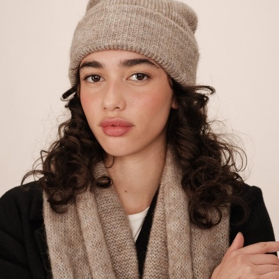 Mulher com gorro e cachecol bege em fundo neutro