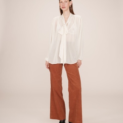 Modelo vestindo camisa branca com laço e calças largas castanho-avermelhadas