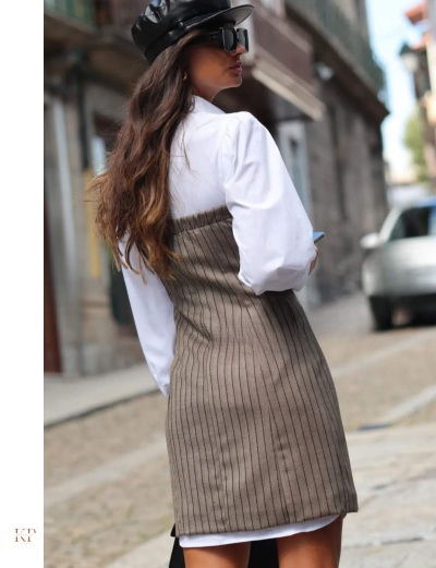 Mulher com vestido cinza às riscas e camisa branca numa rua urbana