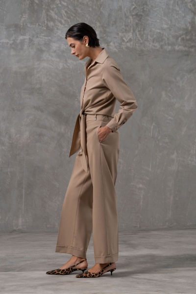 Macacão bege com cinto, calças largas e sapatos de salto baixo com padrão de oncinha em fundo cinzento.